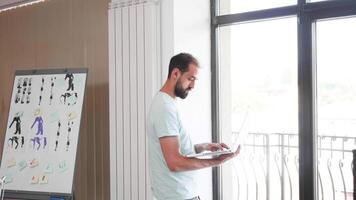 creativo hombre trabajando en su ordenador portátil siguiente a el ventana y Moviente a su escritorio oficina. trabajando en un creativo concepto. video