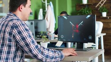 Cheerful young man playing games on his computer while he's at the office. Coworkers in the background. video