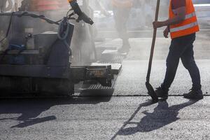 men working with asphalting paver machine during road street repairing works at day light with smoke and steam in the air photo