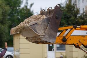 front loader scoop with macadam and worker hand in front of it gesturing to stop photo