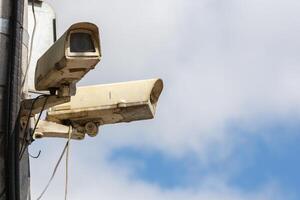 two old CCTV surveillance cameras on street pole at summer day photo