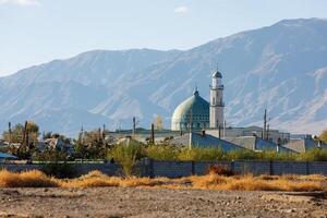 Al Amin mosque in Balykchy, Kyrgyzstan in front of mountains at sunny autumn day photo