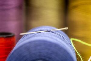 Closeup of a needle in a thread with other colorful needles in the blurry background photo