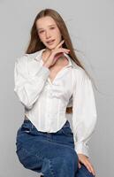 A girl in a white shirt and jeans on a gray background. Seventeen year old beauty. photo