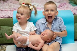 Little brother and sister rejoice at the newborn baby. Three children of different ages in a home environment. The large family. photo