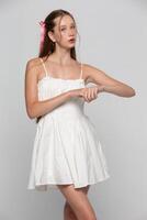 Portrait of a young seventeen-year-old girl in a white short dress on a gray background. photo