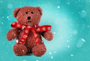 Vintage toy bear with a Christmas bow on an emerald background covered with white snowflakes. photo