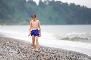 The boy walks along the rocky shore of the sea. photo