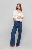 Young girl in jeans and a white shirt on a gray background. photo