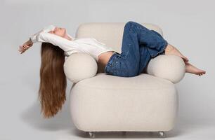 A beautiful slender girl with long blond hair lies in a comfortable white chair. A woman rests and relaxes in a chair. photo