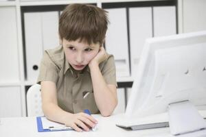 Sad schoolboy does homework. Upset boy behind desk with pen and notebook.The little boy thinks over the task photo