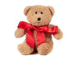 juguete mullido Clásico oso con un rojo arco en un blanco antecedentes. marrón osito de peluche oso aislado. foto