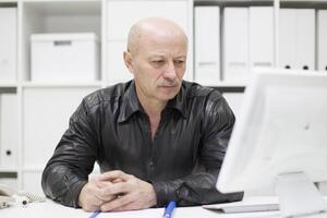 un mayor calvo hombre a el computadora. pensionista en el lugar de trabajo foto