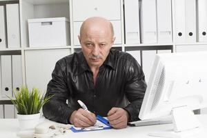 An elderly bald man at the computer. Pensioner in the workplace photo