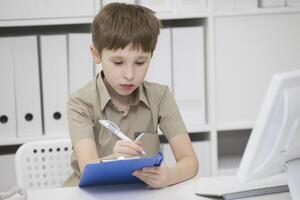 Junior school student does his homework. A boy with a pen in his hands writes something. A child solves a problem photo