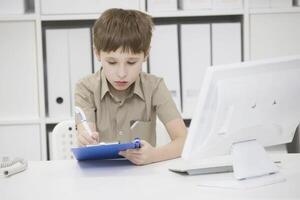 Junior school student does his homework. A boy with a pen in his hands writes something. A child solves a problem photo