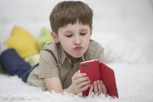 Child with a mobile phone. Schoolboy with a smartphone lying on the bed. Kids and Gadgets photo