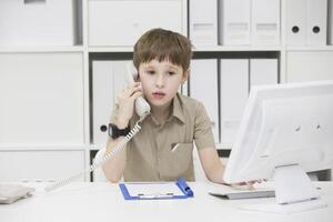 The child at the computer holding the phone.Boy playing businessman photo