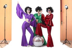 A group of girls with a disco ball in colorful costumes in a photo studio posing on a white background.