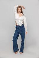 A girl with long white hair in a white shirt and jeans in full length on a gray background. photo