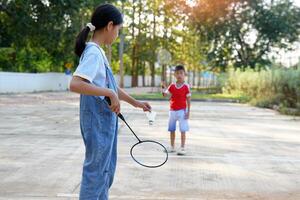 asiático niña y chico jugar bádminton al aire libre a el parque juntos en vacaciones. suave y selectivo enfocar. foto