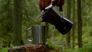 Coffee is poured into a mug from a coffee maker. Beautiful forest on the background. Travel concept Ultra 4K photo