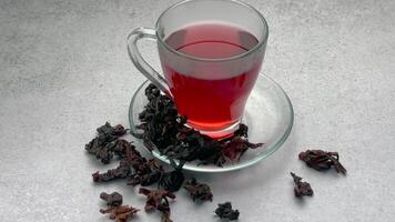 Red hibiscus tea in a glass cup and dried hibiscus flowers on the table video