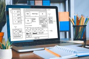 Digital and paper wireframe designs for web or mobile app UI UX display on laptop computer screen. Panoramic shot of developer workspace for brainstorming and design application framework. photo