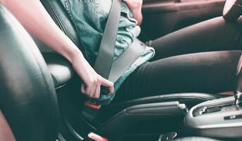 el mujer mano es pegado con un asiento cinturón a comienzo conducción en el coche. de cerca imagen de un mujer sentado en coche y poniendo en su asiento cinturón foto