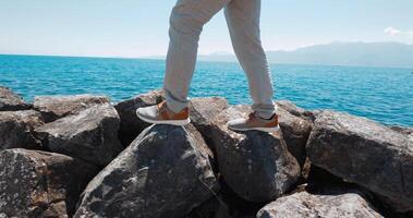 hombre caminando en Roca en el mar exterior. ver de piernas con marrón Zapatos cerca arriba foto