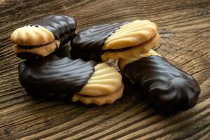 Cookies on wooden table. Biscuits with filling on wooden desk. Sweet cookies dipped in chocolate. photo