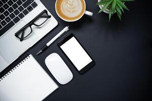 Top view with laptop, mobile phone, coffee cup, pencil, pencil and glasses placed on a black background photo