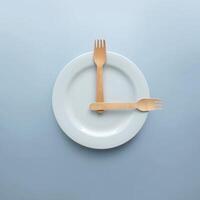 Top view of Spoon and fork on white round plate in a form of clock on blue background. Minimal food idea concept. photo