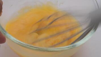 Hand whisking eggs. Beating chicken eggs in glass bowl with manual mixer close up. video