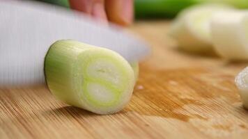 Woman's hand holding a knife cutting fresh Japanese scallions on a wooden chopping board. Sliced leek or Chopped green japanese bunching onion on a wooden board. video