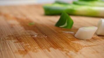 Woman's hand holding a knife cutting fresh Japanese scallions on a wooden chopping board. Sliced leek or Chopped green japanese bunching onion on a wooden board. video