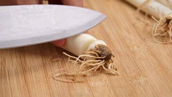 Woman's hand holding a knife cutting fresh Japanese scallions on a wooden chopping board. Sliced leek or Chopped green japanese bunching onion on a wooden board. video