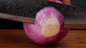 Female hand holding a knife and slicing onions on a wooden cutting board. Cutting big shallots  close up. video