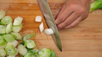 Woman's hand holding a knife cutting fresh Japanese scallions on a wooden chopping board. Sliced leek or Chopped green japanese bunching onion on a wooden board. video