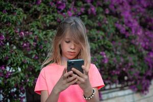 a young girl is using her phone while standing in front of a bush photo