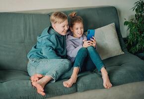 two children sitting on a couch looking at a phone photo