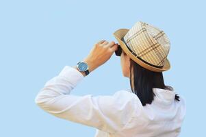 A brunette woman in sunglasses, a white shirt and a straw summer hat looks into the distance. Elegant woman - traveler. photo