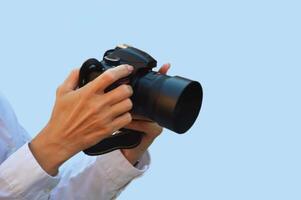 A female photographer in a white shirt holds a digital camera in her hands. Isolate on a blue background. Free space for text. photo