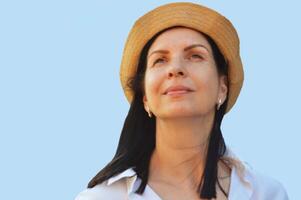 retrato de un caucásico morena mujer vistiendo un verano sombrero y blanco camisa, aislado en un azul antecedentes. foto