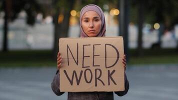 Sad muslim woman in hijab standing outdoors islamic ethnic girl upset unemployed worry stressful lady poor female showing holding cardboard banner sign need work, dismissal pandemic covid crisis photo