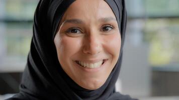 Headshot of young attractive arab woman in hijab looking at camera beautiful muslim girl with natural make-up posing indoors portrait happy islamic female smiling with healthy white teeth close-up photo