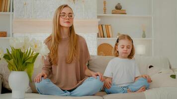 Caucasian woman mom with little child girl sitting home at couch in lotus position closed eyes meditate together. Family meditating mother teach meditation small daughter adorable baby kid breath photo