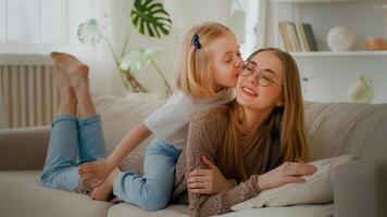 contento maternidad familia unión cariñoso amor caucásico madre acostado en sofá sofá hija pequeño niña niño a cuestas Beso mamá besos encantador padre calentar comunicación hablando dulce sensibilidad foto