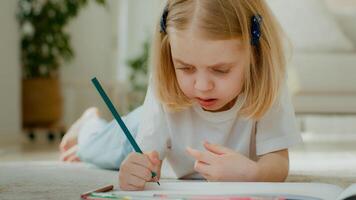 Cute concentrated Caucasian little kid girl draw color pencil lying on floor at home play alone. Talented preschool child daughter kid baby coloring picture at home drawing painting creative paint photo