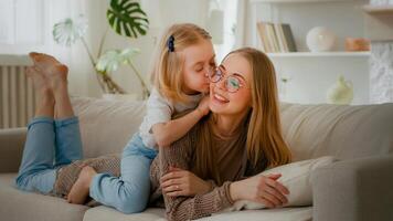 contento maternidad familia unión cariñoso amor caucásico madre acostado en sofá sofá hija pequeño niña niño a cuestas Beso mamá besos encantador padre calentar comunicación hablando dulce sensibilidad foto